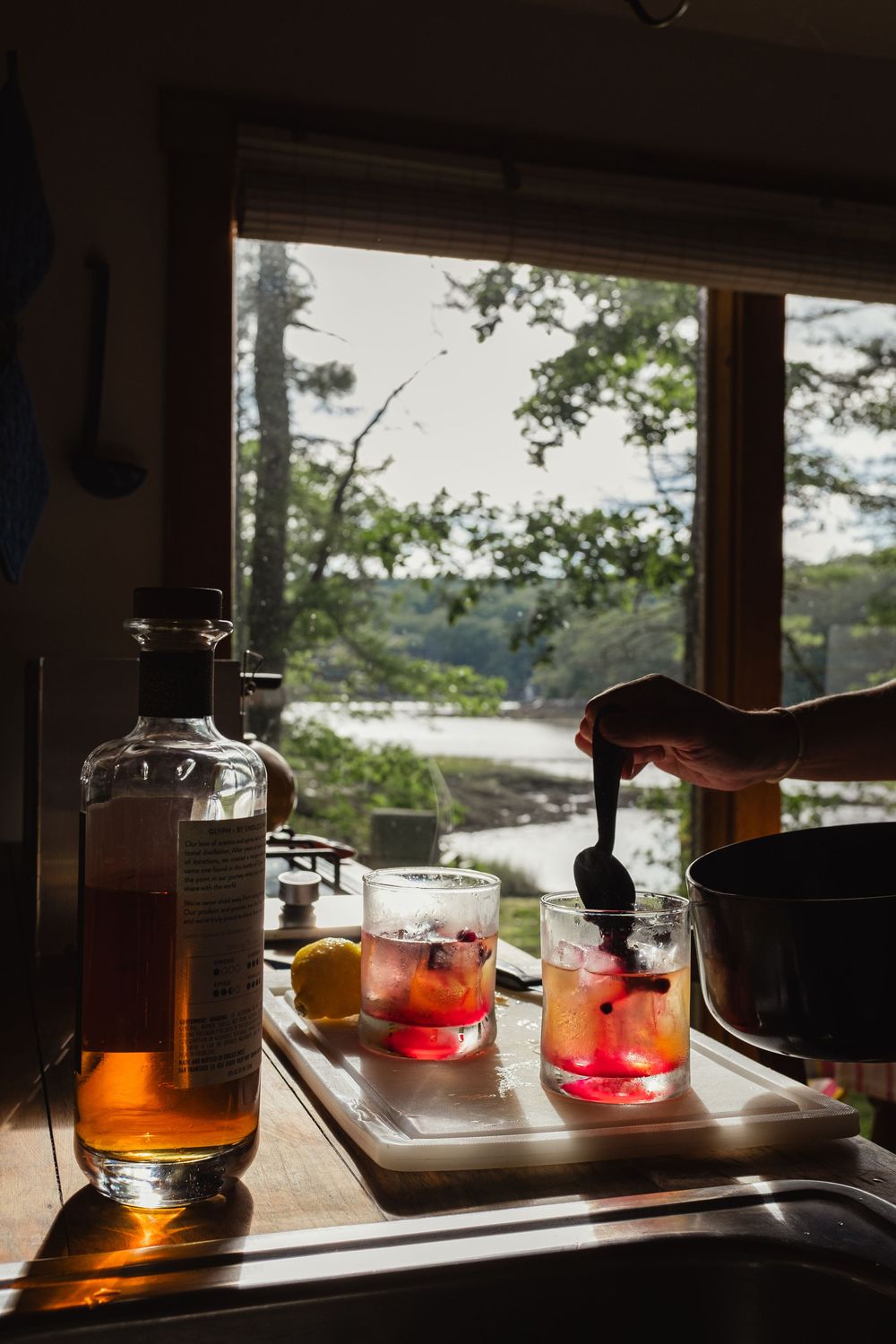 Glass bottles and containers sit silhouetted on a wooden windowsill with sunlight streaming through the window.