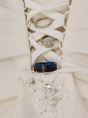 Wedding rings and engagement rings artfully displayed through white dress lacing details and beaded embellishments.
