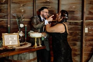 Playful cake cutting moment between newlyweds at a rustic wooden venue.