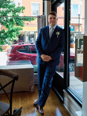 Someone in a navy blue suit stands in front of a window in a restaurant or cafe, with a red car visible outside.