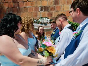 Bridesmaids in light blue dresses and groomsmen in formal attire gather during cheerful outdoor wedding ceremony.