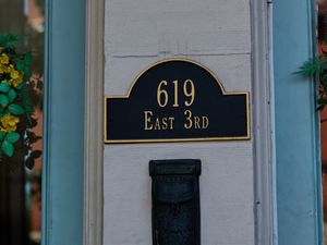 Four close-up photographs showing black house number plaques mounted on light-colored exterior walls.