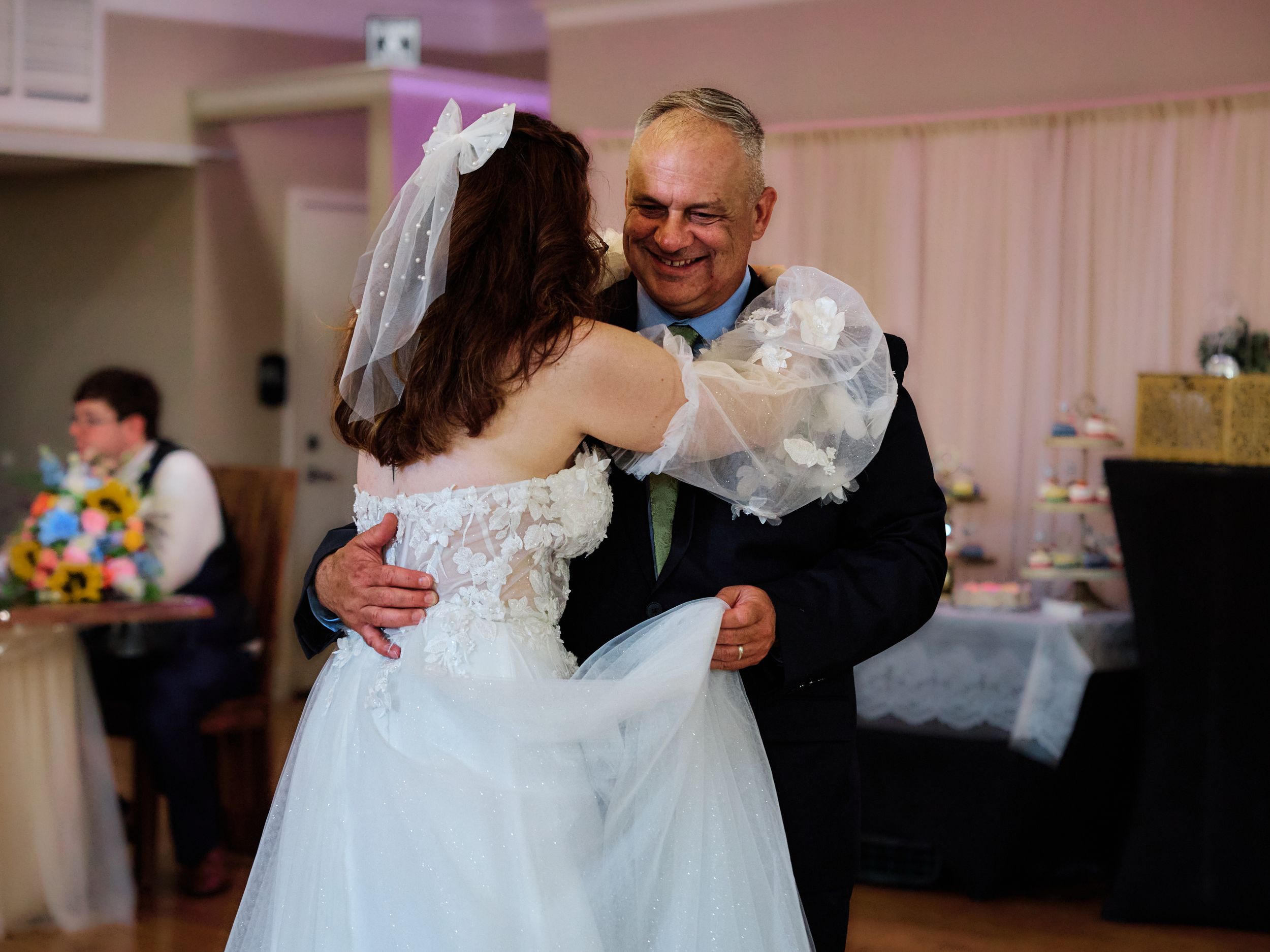 A heartwarming dance moment between two people at a wedding reception in a pink-lit ballroom.
