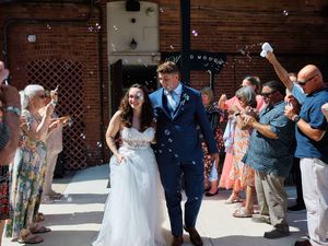 Wedding guests cheer and celebrate as newlyweds dance together during an outdoor celebration at a brick venue.