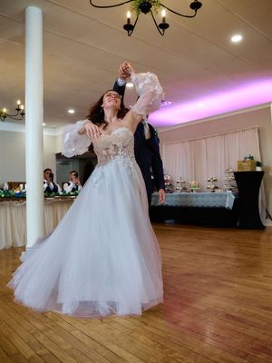 Couple dances elegantly at their wedding reception, with bride in white tulle gown twirling on wooden dance floor.