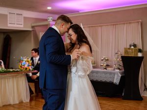 A couple shares a romantic first dance at their wedding reception under purple lighting.