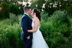 A couple shares an intimate moment in formal attire against a lush green background.