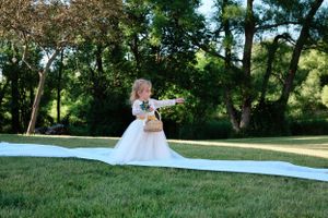 A person in a flowing white wedding dress poses outdoors in a grassy setting.