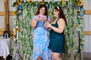 Two guests in formal attire enjoying drinks at a wedding reception with a sunflower backdrop.
