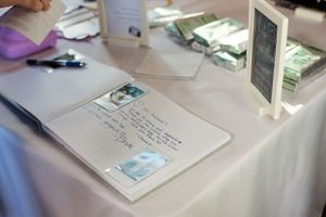 Wedding guest book and photos displayed on white linen table at reception.