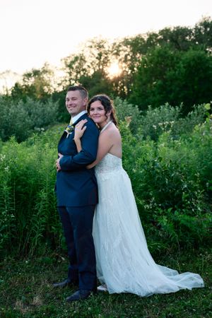 A couple poses for a romantic portrait in a field at sunset in wedding attire.