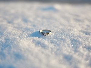 A sparkling diamond engagement ring rests delicately in powdery white snow with shallow depth of field.