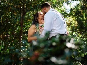A romantic outdoor engagement photo shoot framed by lush green foliage.