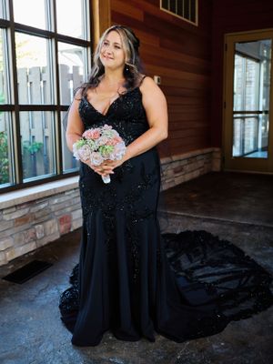 Elegant black sequined gown with a flowing train and pastel bouquet in rustic indoor setting.