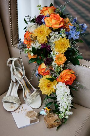 Vibrant wedding bouquet with orange roses and yellow dahlias displayed next to bridal shoes.