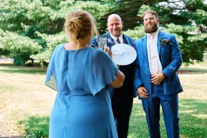 An outdoor wedding ceremony scene with attendees in blue and formal attire.