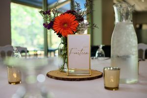 An elegant wedding centerpiece featuring an orange gerbera daisy in a vase with table number.