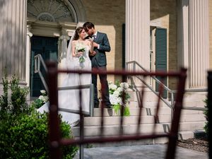 A romantic wedding moment captured on an elegant porch with white columns and greenery.