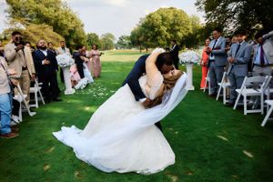 A romantic wedding dip kiss captured during an outdoor ceremony with guests watching.