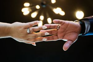 Two hands displaying wedding rings touch against a backdrop of glowing bokeh lights.