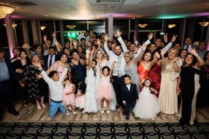 Large group of wedding guests pose together for a celebratory photo with raised arms and excited expressions.