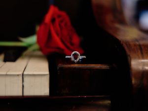 A diamond engagement ring sits on piano keys beside a red rose in a romantic composition.