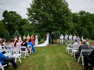 Panoramic view of white chairs set up on a grassy hillside for an outdoor wedding ceremony under green trees.