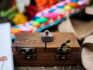 A vintage wooden jewelry box with ornate metal clasps and decorative key holder sits on a textured surface.