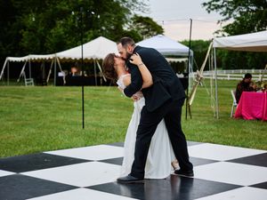 A couple dances together on a black and white checkered dance floor under outdoor event tents on a grassy lawn.