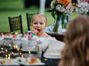 A group gathers around a festive table at an outdoor celebration with fairy lights and dining chairs.