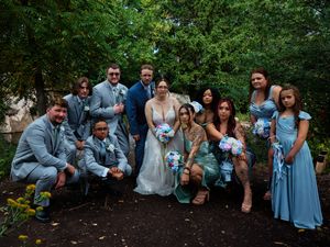 A group of wedding guests in light blue attire gather outdoors in a garden setting during a celebration.