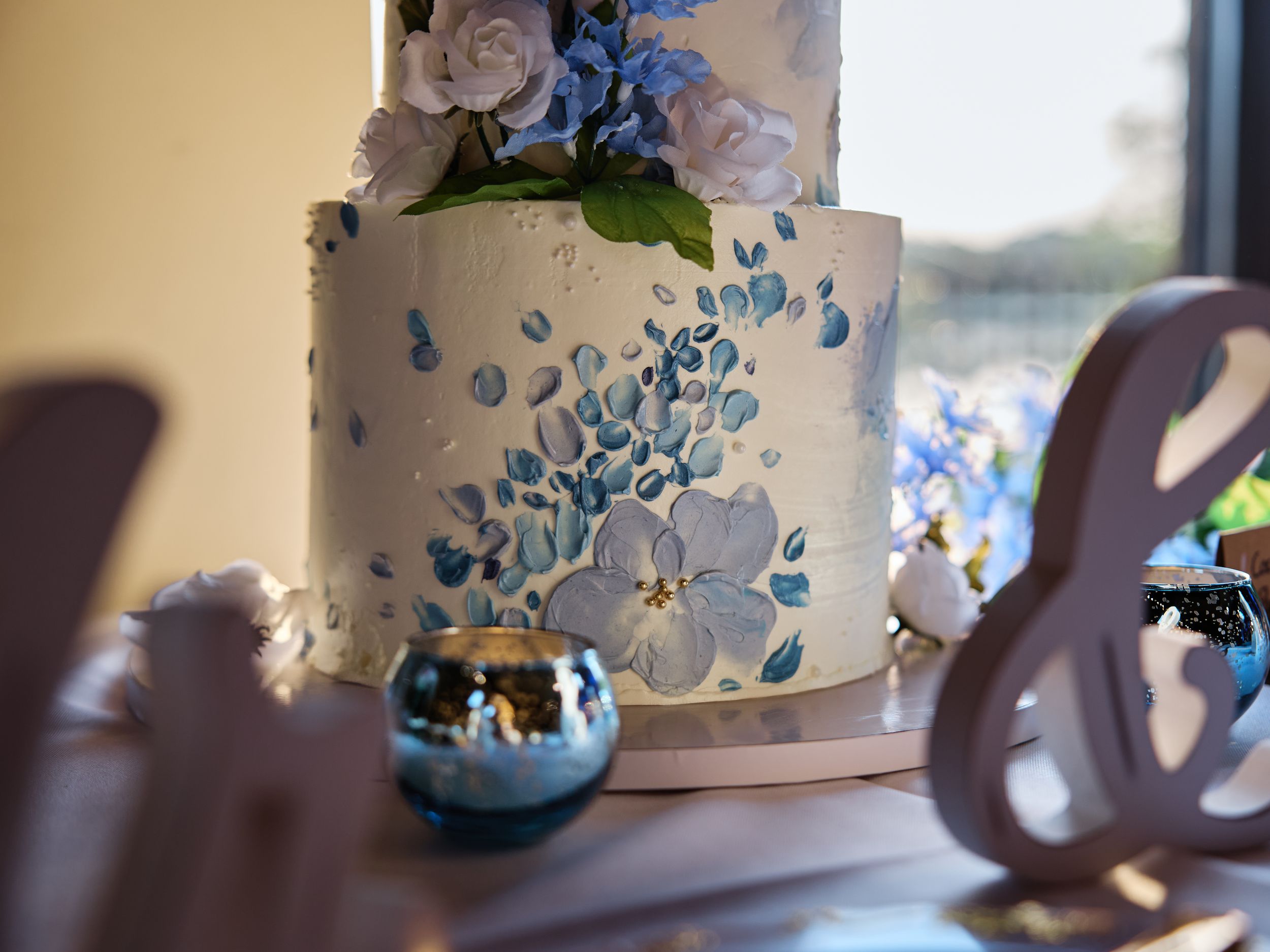 A white wedding cake decorated with delicate blue floral details and silver accents sits elegantly on display.