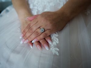 Close-up view of hands with pink manicured nails resting on delicate white lace fabric.