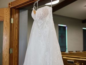 A detailed lace wedding dress hangs gracefully on a wooden door frame.