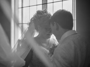 A black and white portrait of a couple in an intimate moment by a window.