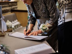 Wedding document being signed with a white floral boutonniere on display.