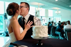 Reception moment with wedding cake in foreground and teal-tinted venue lighting.