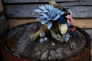 A rustic wedding bouquet with blue and pink flowers arranged on a wooden surface.