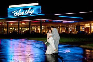 Newlyweds embrace outside illuminated Blue Dog restaurant with neon signage at night.