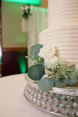 White wedding cake detail with eucalyptus leaves and crystal stand decoration in green ambient lighting.