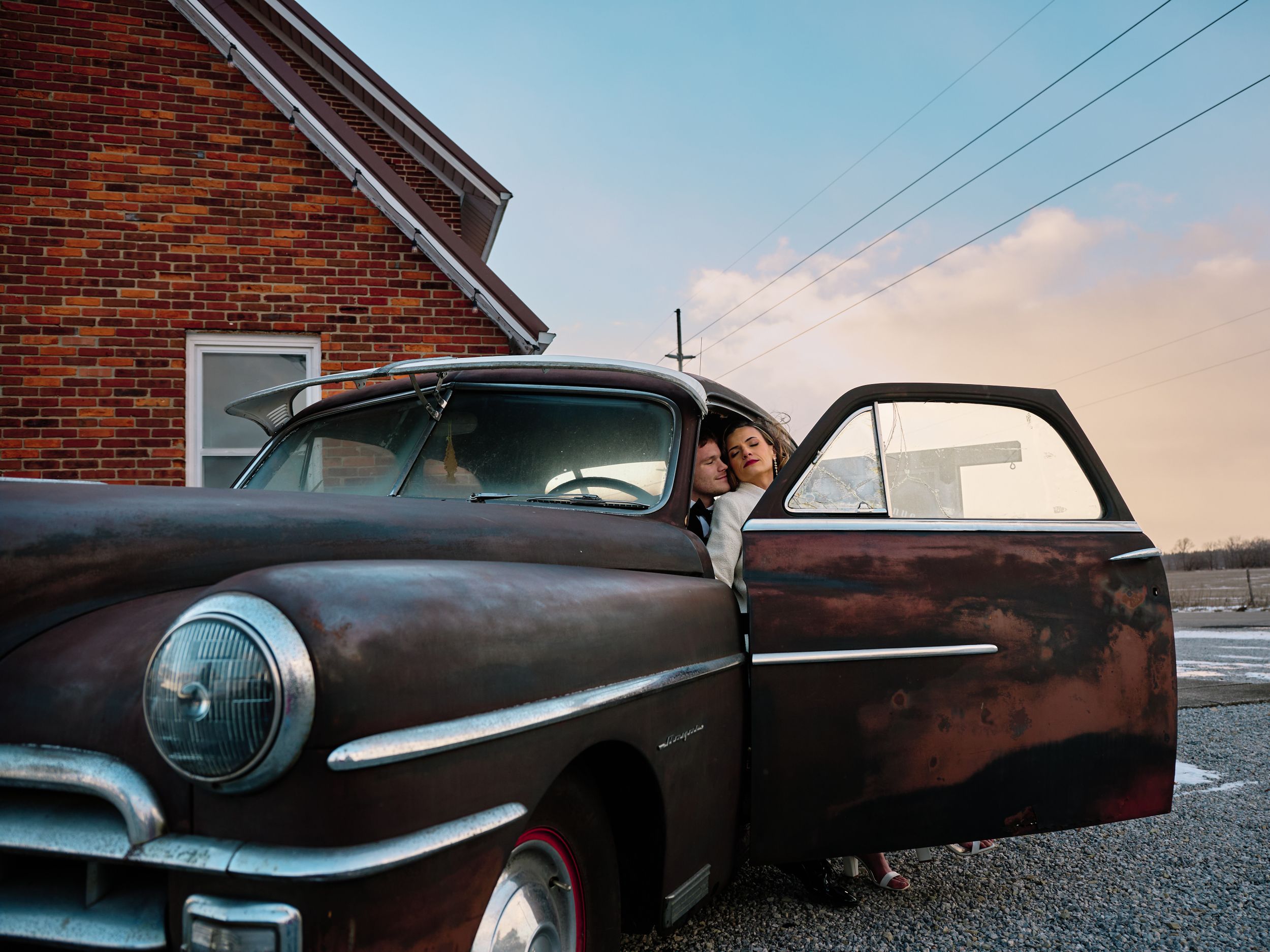A vintage Chrysler automobile with open door parked outside a brick building at dusk.
