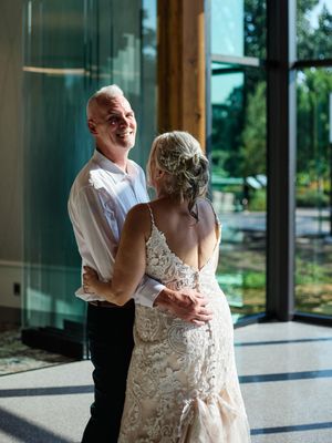 A couple shares a tender first look moment in a sunlit venue with floor-to-ceiling windows.