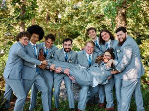 A playful wedding party in matching light blue suits posing together outdoors.
