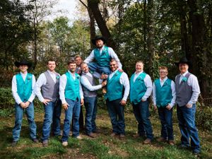 A wedding party in turquoise vests and grey shirts poses outdoors.