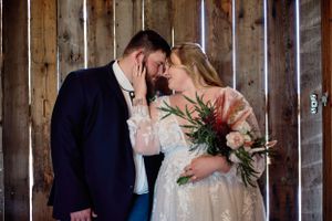 A romantic wedding moment captured in a rustic barn setting with a beautiful bouquet and elegant attire.