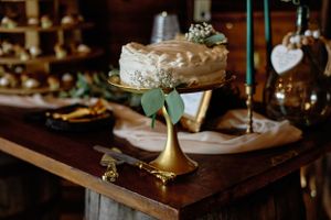 An elegant wedding cake displayed on a gold pedestal with eucalyptus leaves and rustic decorative elements.
