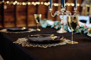 Elegant place setting with gold charger plate and wine glass on black tablecloth with bokeh background.