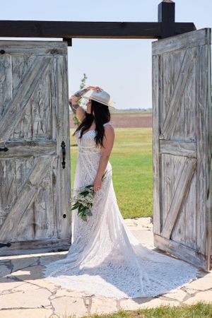 Bride in lace gown poses between rustic barn doors with flowing train and bouquet.