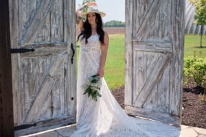 Bride in lace gown poses in rustic doorway of weathered white barn doors.