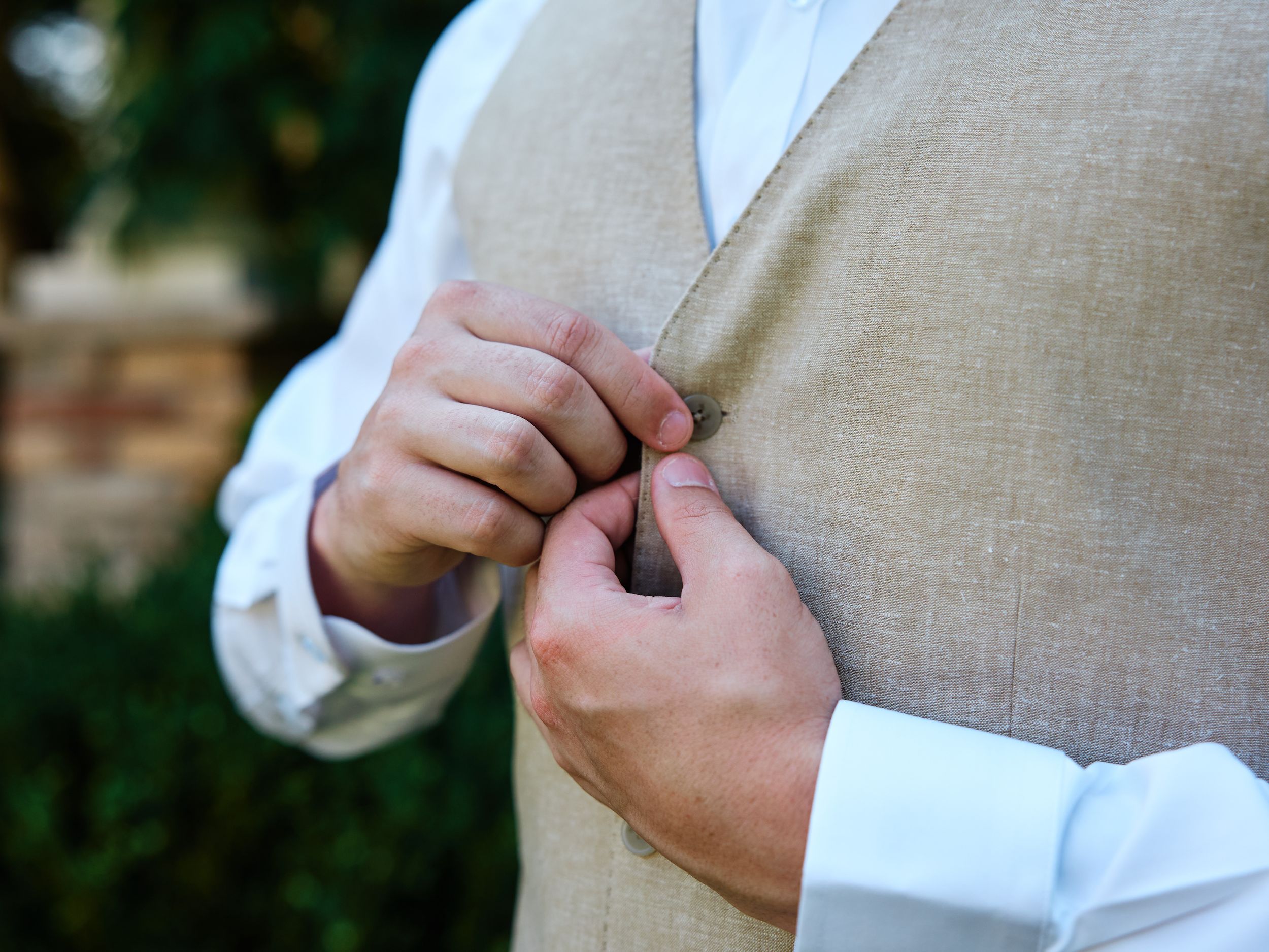 A groom adjusts the sleeve of his light beige suit jacket during a formal event.